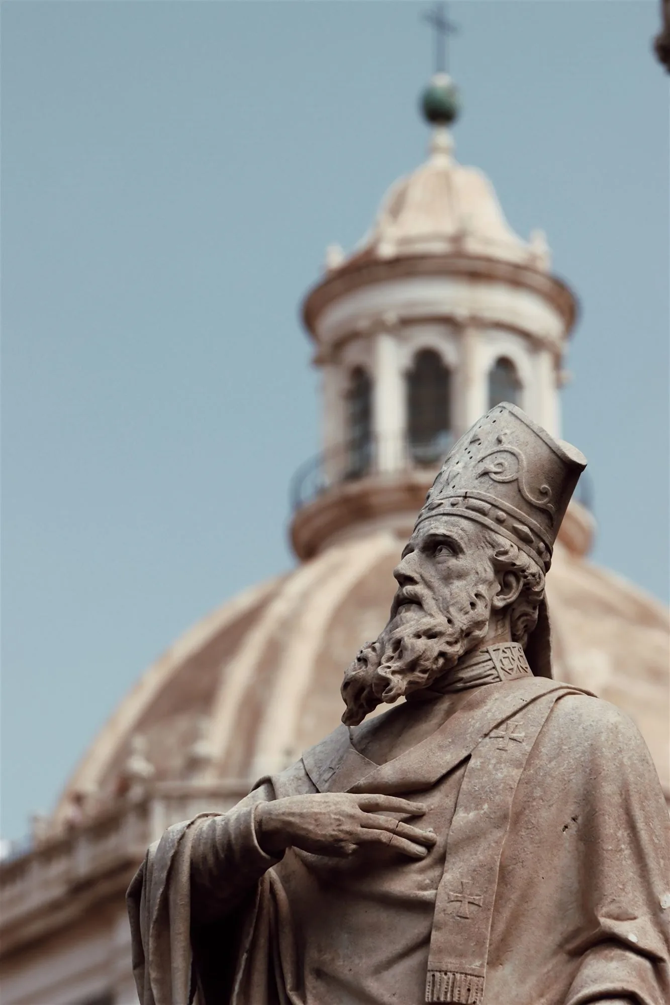 Stone statue of a bishop before a church dome