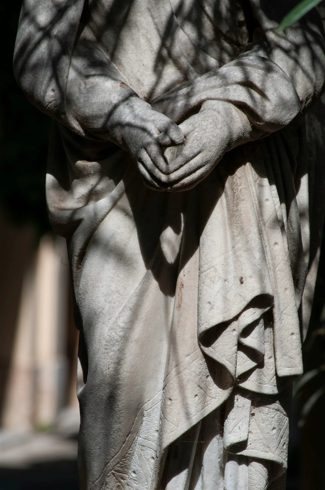 Hands of a stone figure folded in prayer